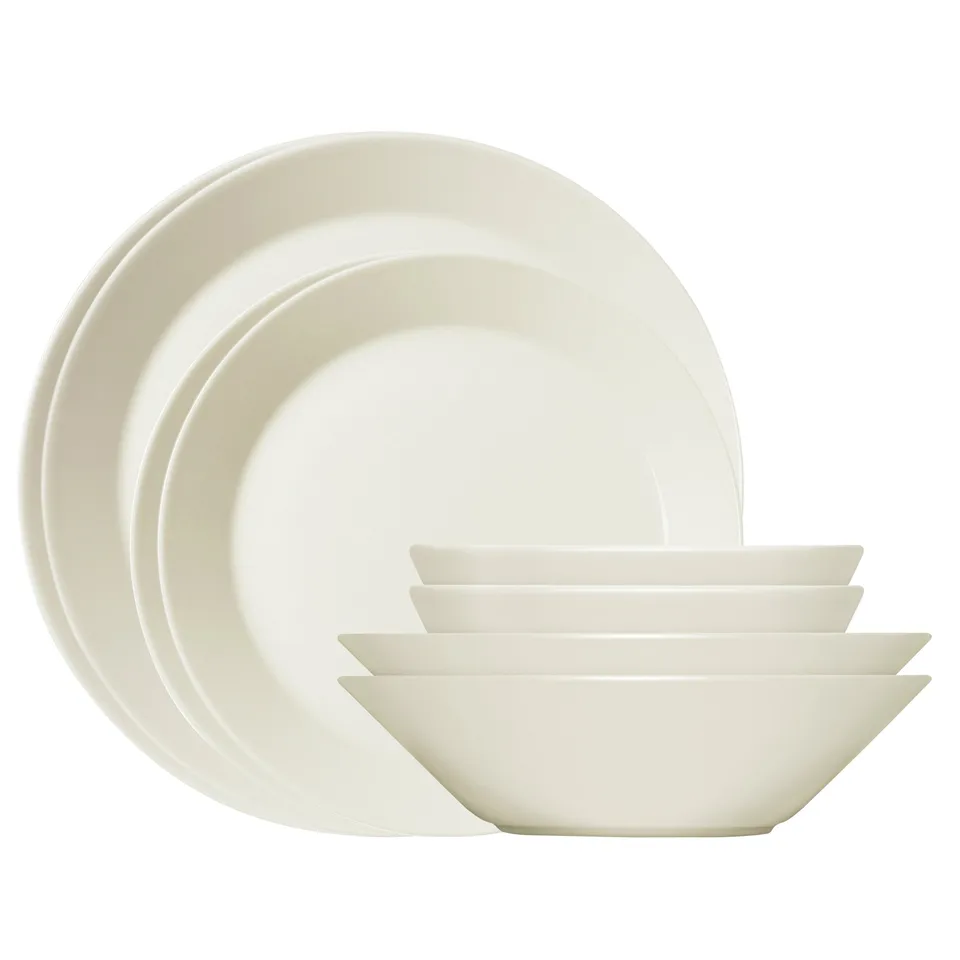 Tre runde tallerkener stillet på højkant bag tre stablede dybe skåle i cremehvidt porcelæn på hvid bund