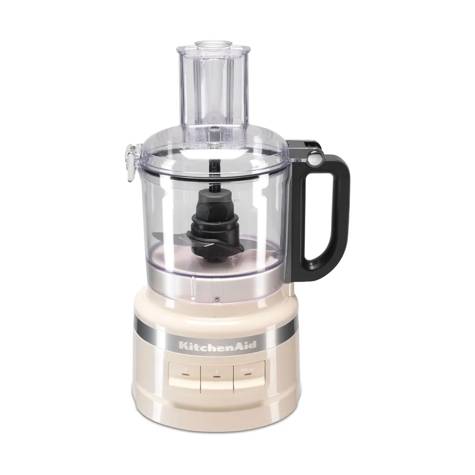 Foodprocessor med cremefarvet fod og KitchenAid-navn, klar skål med kniv i og et påfyldningsrør på toppen, på hvid bund