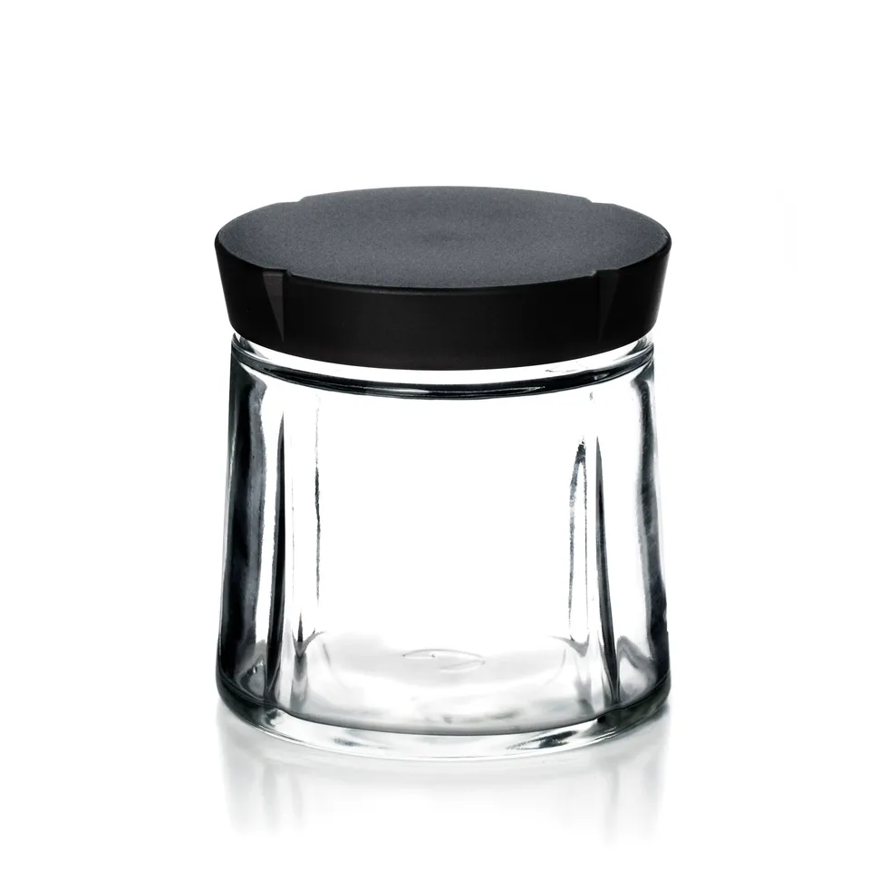 Lav, bred krukke i klart glas med et tykt mat sort låg, på hvid bund