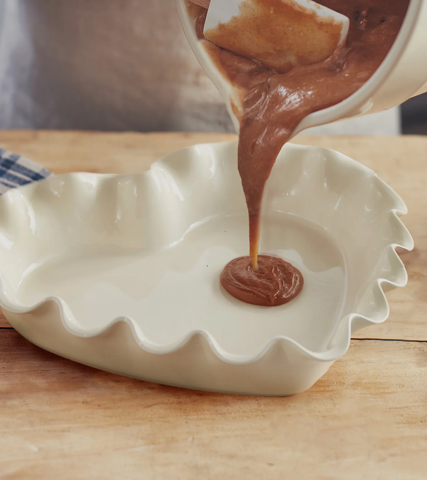 Hælder chokoladedej fra en skål i en hjerteformet bageform på et træbord.