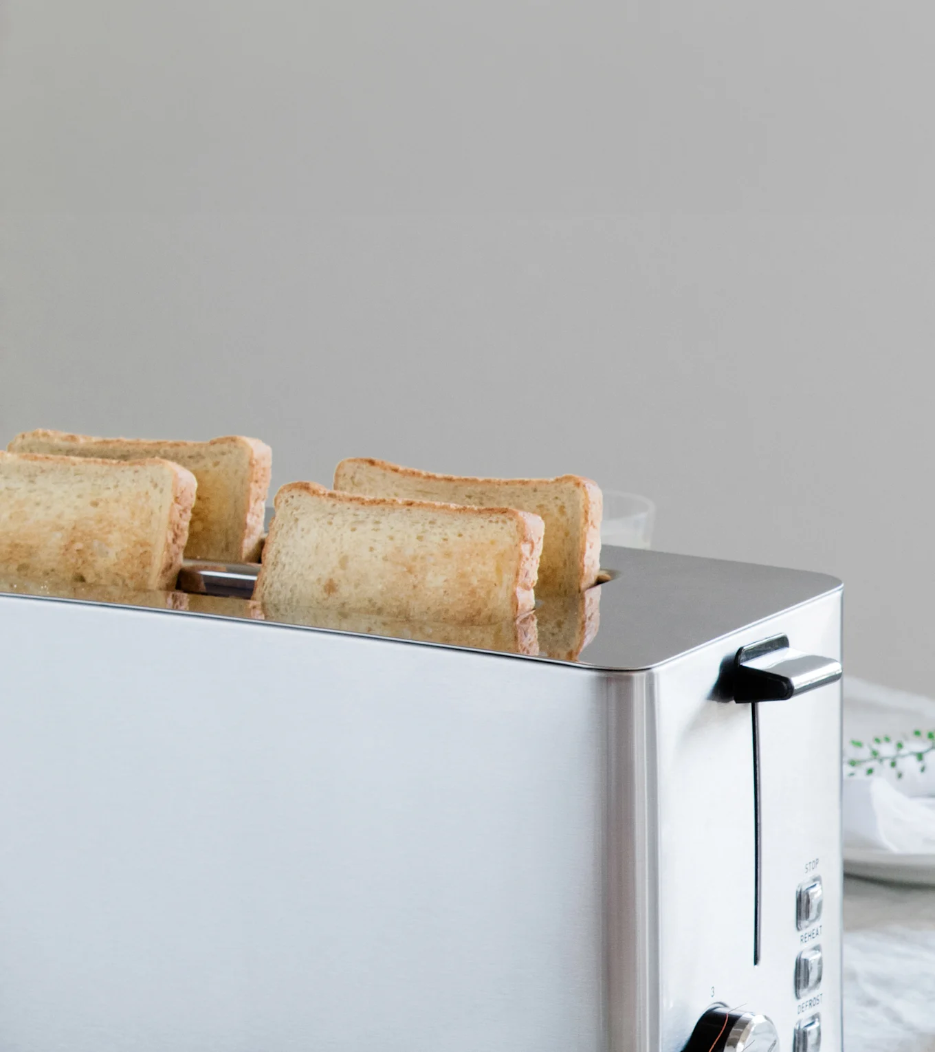 En sølvfarvet brødrister med fire skiver let ristet brød, der delvist er kommet op af dens åbninger.