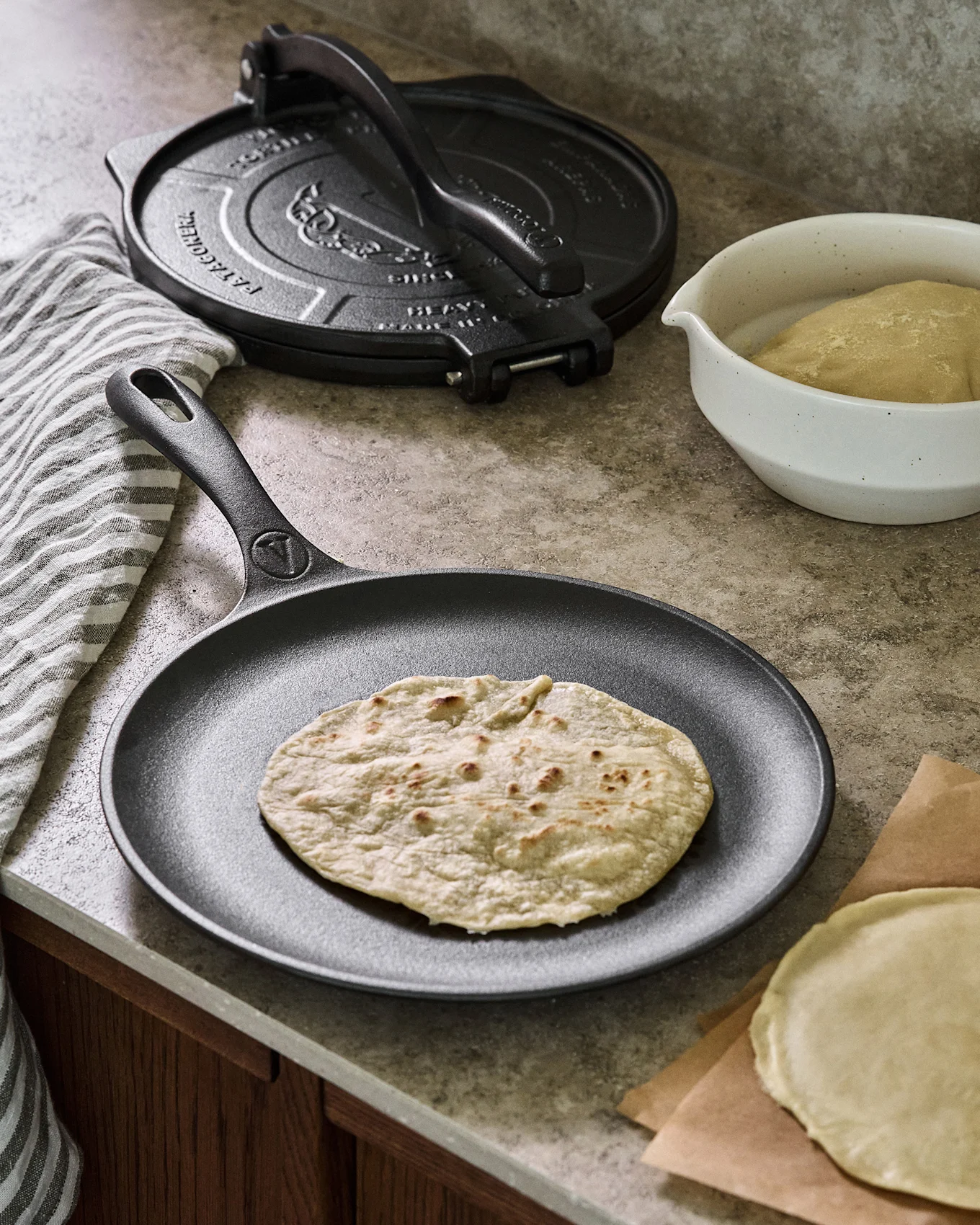 Støbejernspande med fladbrød, ved siden af en tortillapresser og dej.