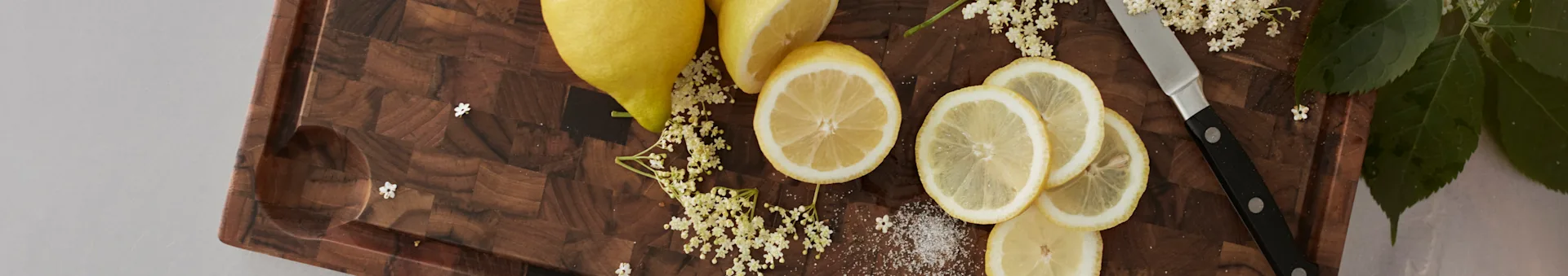 Citroner, hyldeblomster og sukker på et træskærebræt med en kniv.
