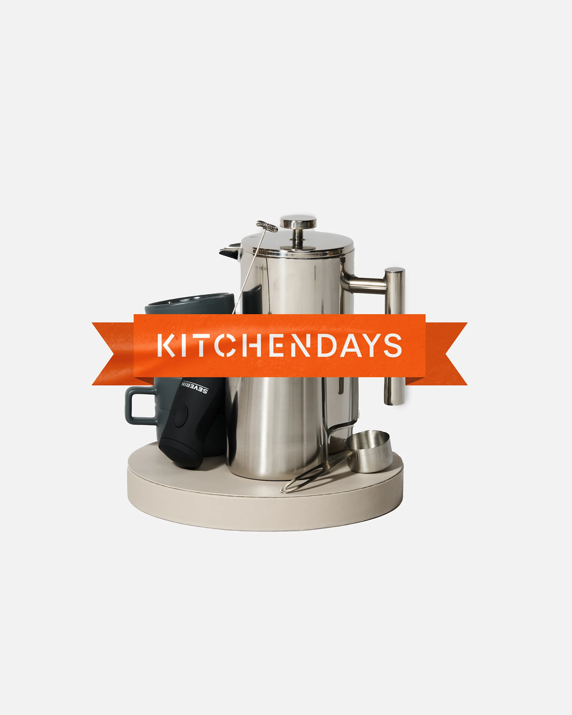 Køkkenudstyr med stålkaffekande, mørke krus, mælkeskummer og måleske på bakke. Orange banner: 'KITCHENDAYS'.