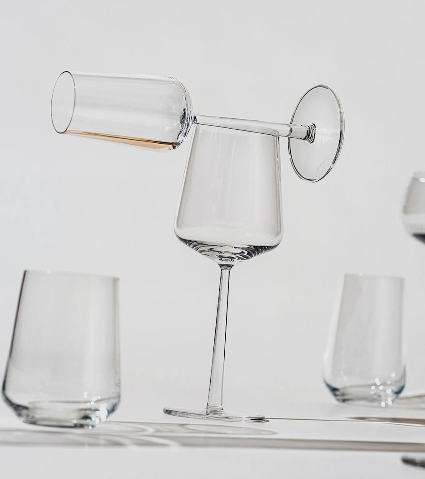 En champagnefløjte med ravfarvet væske balancerer vandret på kanten af et opretstående vinglas, med andre klare glas i baggrunden.