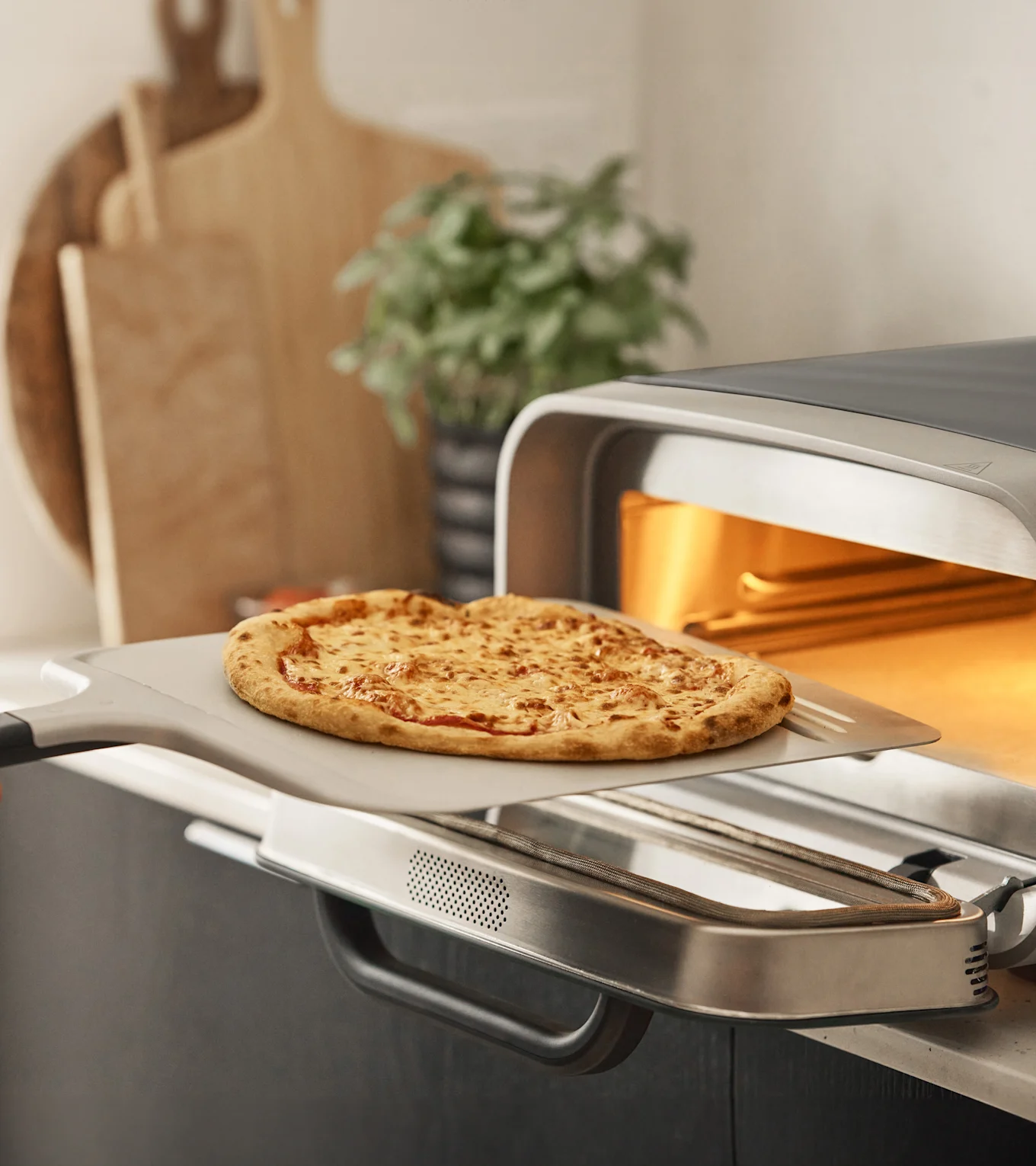 En gylden ostebagt pizza på en spade placeres i en varm, moderne pizzaovn i et køkken.