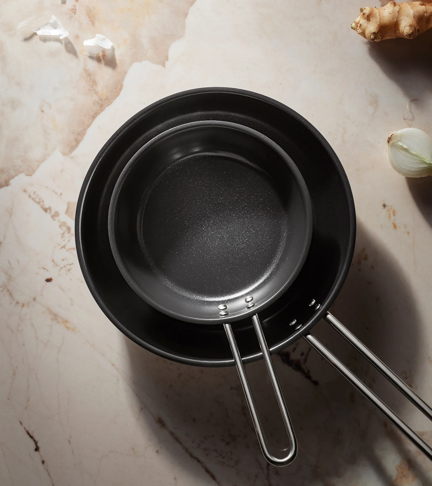 To sorte non-stick stegepander, den ene inden i den anden, på en marmoroverflade.